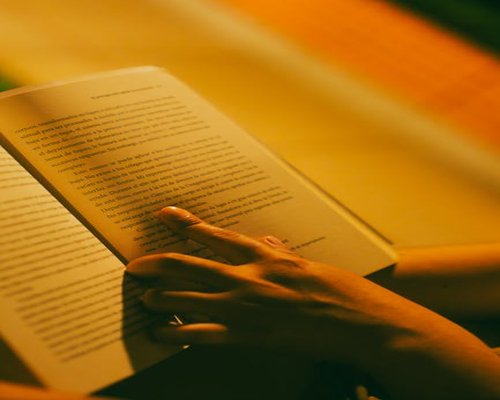 A person reading a book at night with a warm yellow desk lamp illuminating the pages