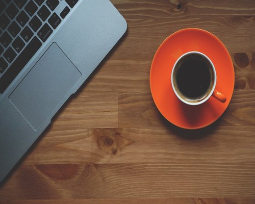 A cup of coffee on a desk with blurred computer screen in the background, implying a break